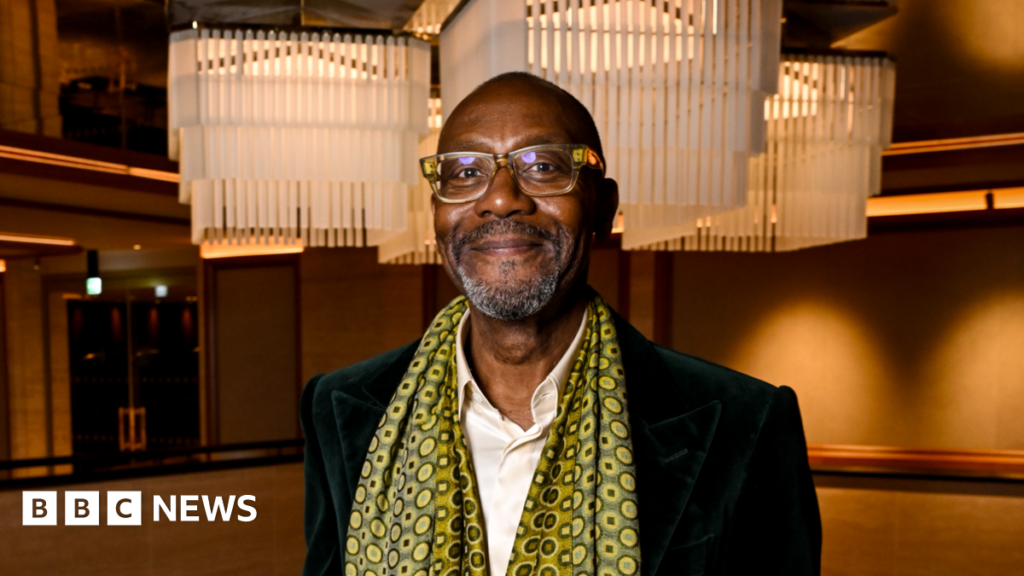 Sir Lenny excited to bring comedy tour back to Dudley A man with short dark hair, a white shirt and dark jacket with a patterned yellow and black scarf around his neck and brown walls behind him