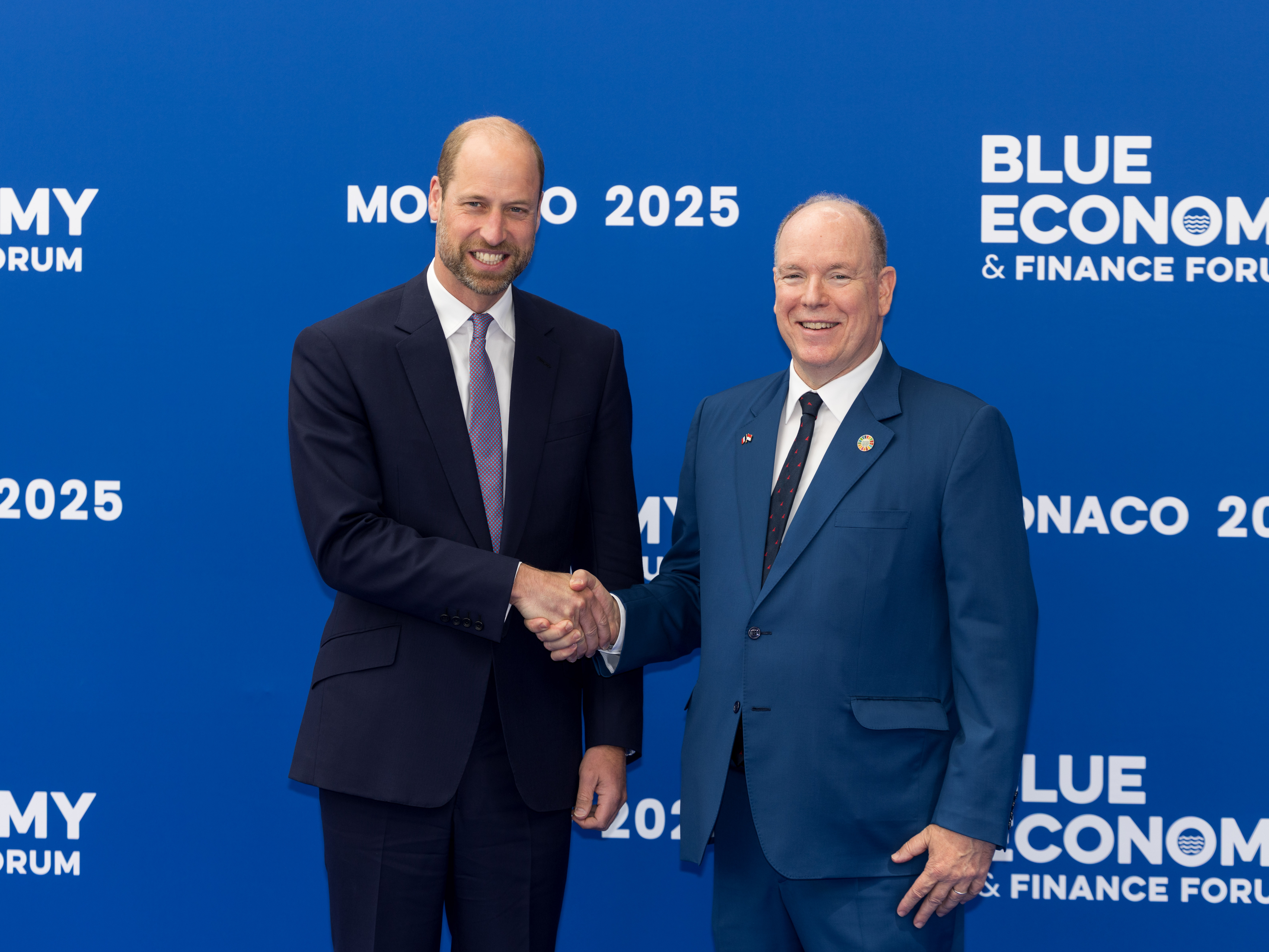 Prince Albert and Prince William shaking hands in front of a step and repeat