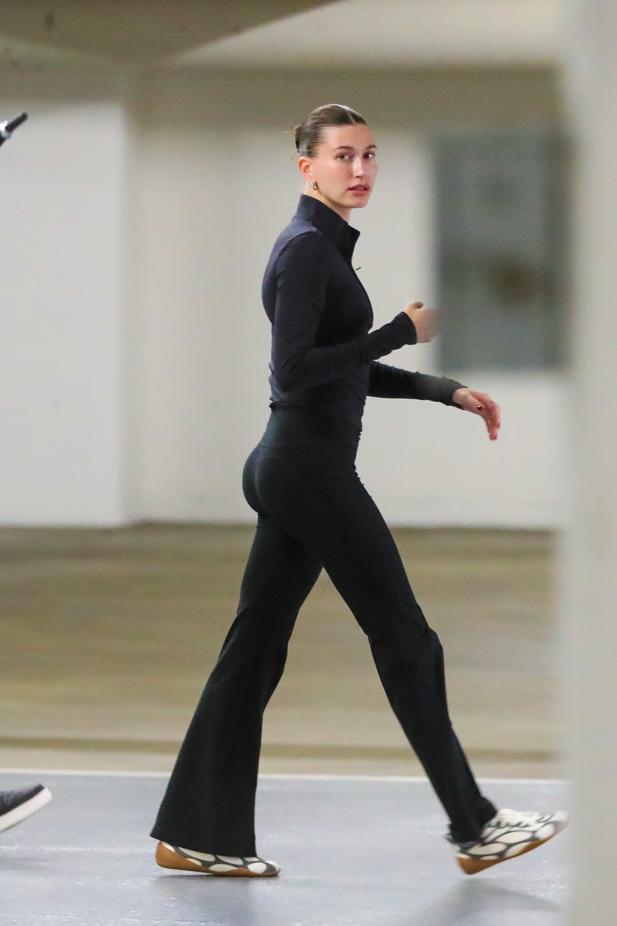 An image of Hailey Bieber wearing a zip-up to, black flare leggings and trainers.