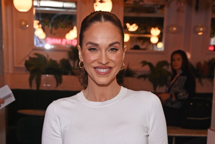 Brunette woman wearing white t-shirt smiles widely at camera.