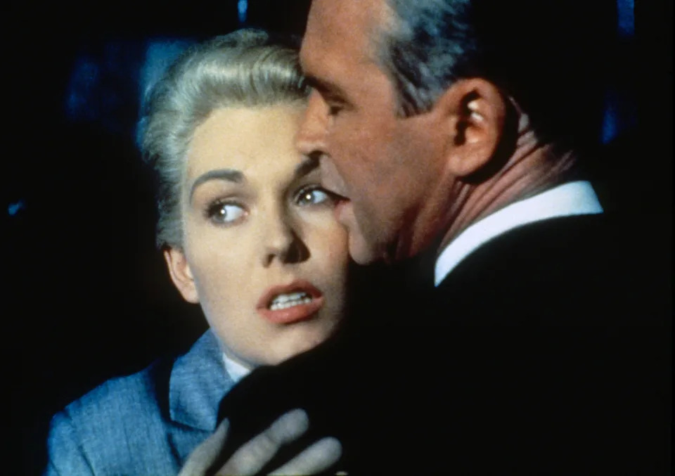 A dramatic scene from a classic film with a woman looking startled, embraced by a man, conveying tension and suspense