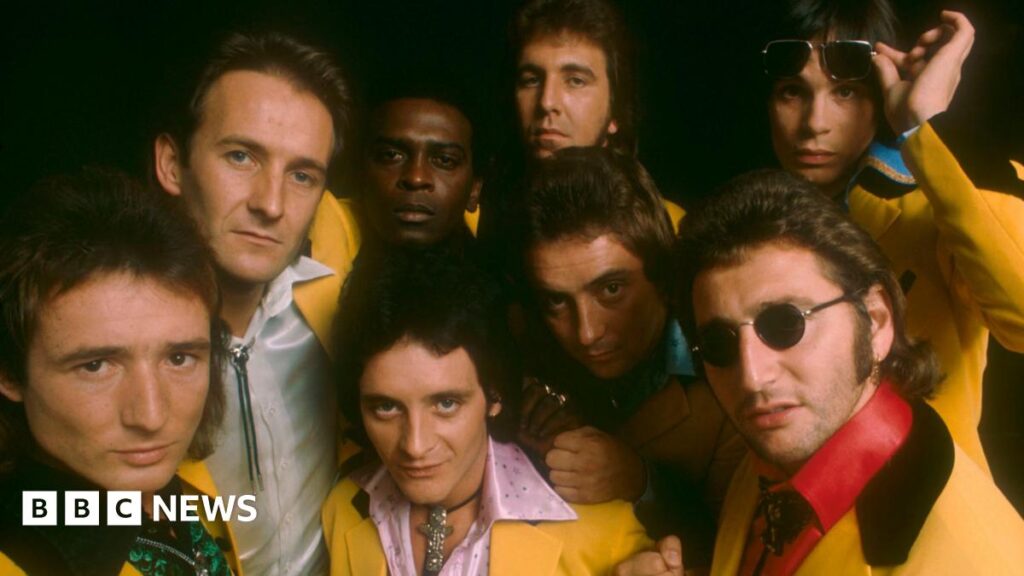 The members of Showaddywaddy dressed in yellow suits looking at the camera.