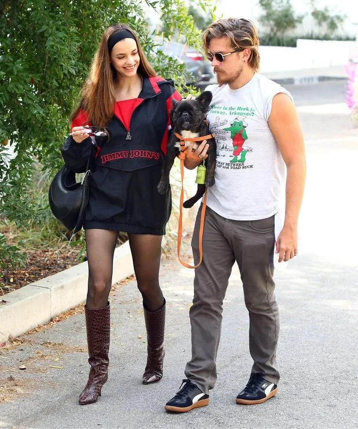 A woman in a casual sporty outfit and a man in a sleeveless shirt walk a small dog, smiling and enjoying a casual moment outdoors