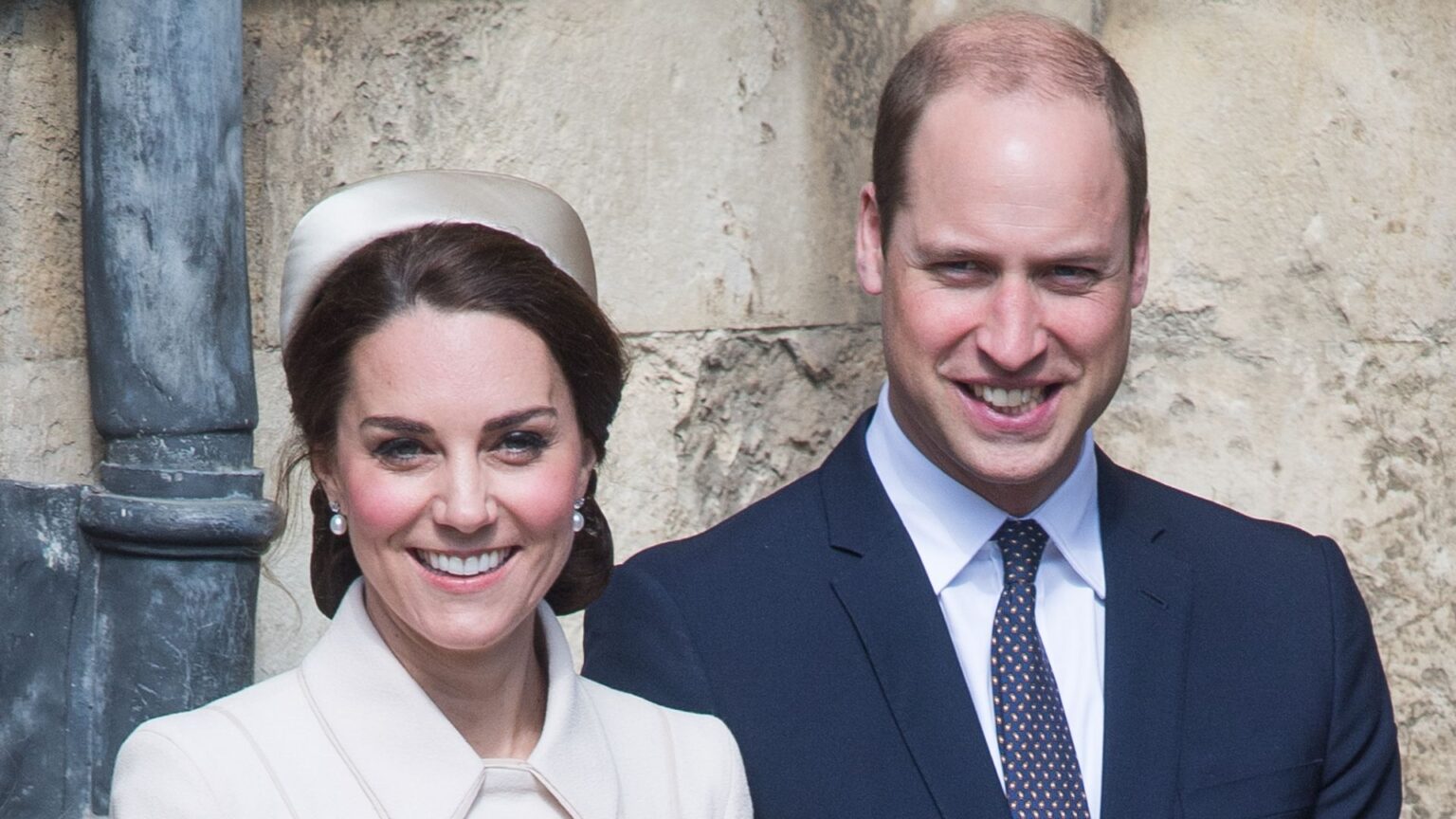 Princess Kate wears a white coat and matching hat while her husband wears a navy suit