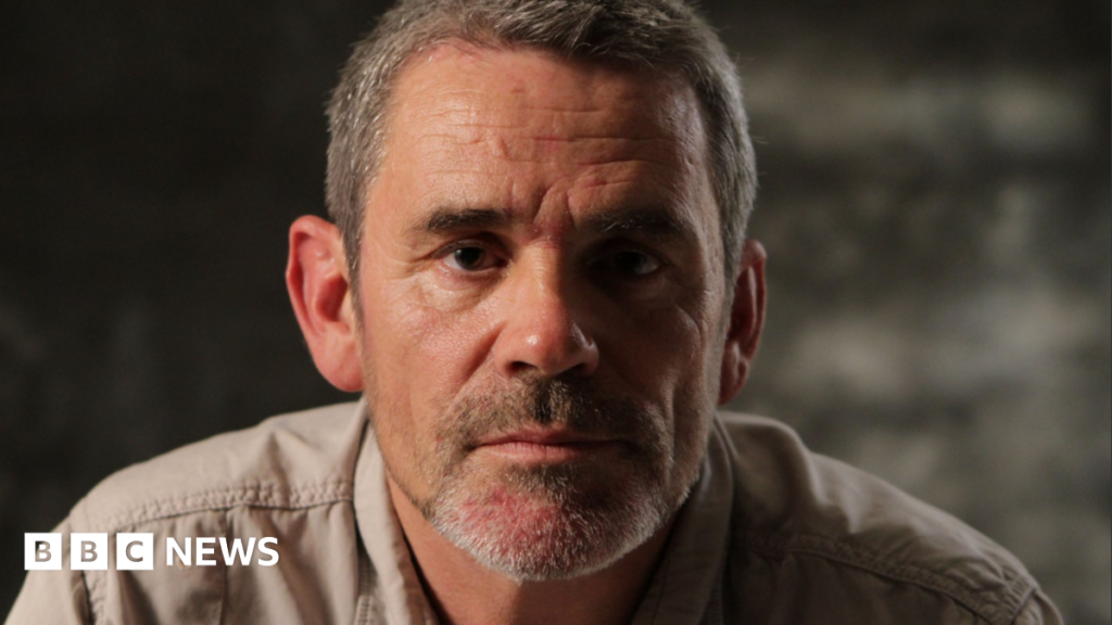 Paul Conroy poses for a headshot. He has short greying hair and stubble.