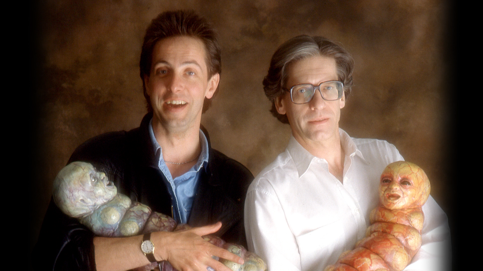 A photo of Clive Barker and David Cronenberg holding horrible baby monsters.