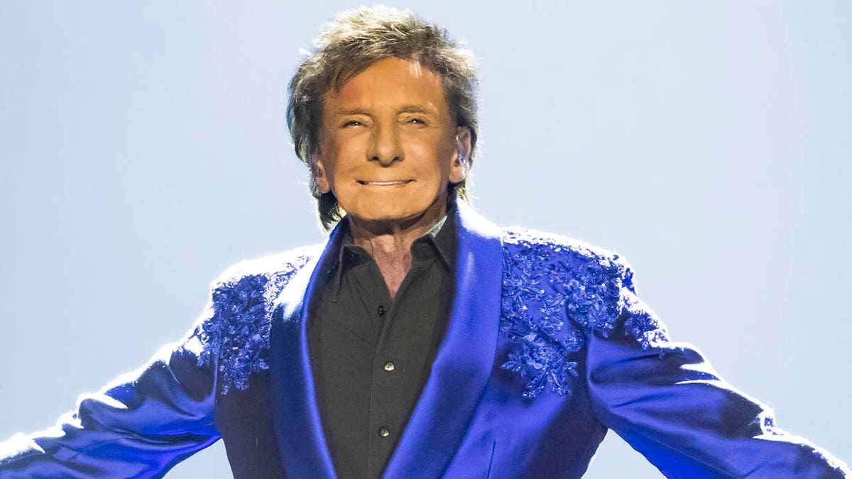 Barry Manilow smiling and spreading his arms out on stage