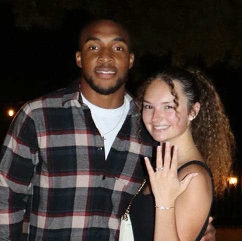 Two people posing together against a backdrop of illuminated letters and rose petals. Two people posing together against a backdrop of illuminated letters and rose petals.
