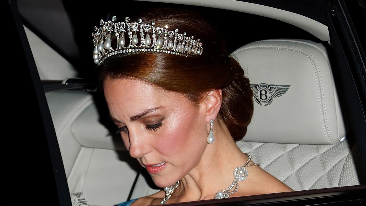 A close-up of Kate Middleton looking down inside a car wearing a tiara.