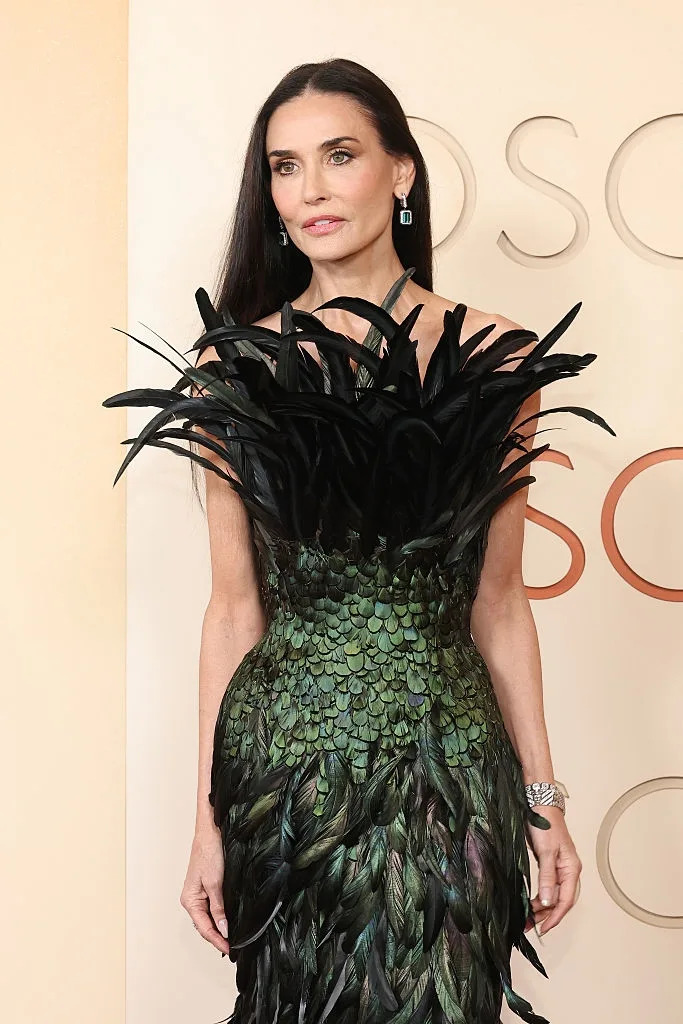 A woman on the red carpet wears an elaborate dress with feather-like details resembling dark plumage