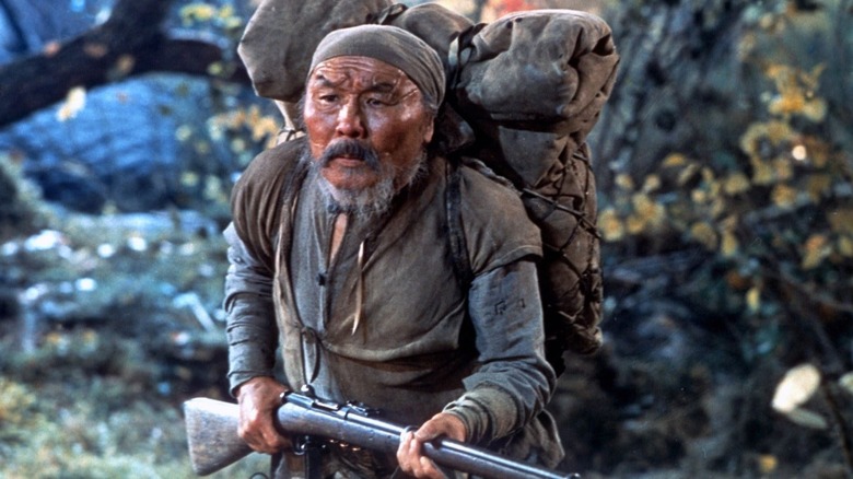 Dersu with a rifle and a backpack in the woods in Dersu Uzala