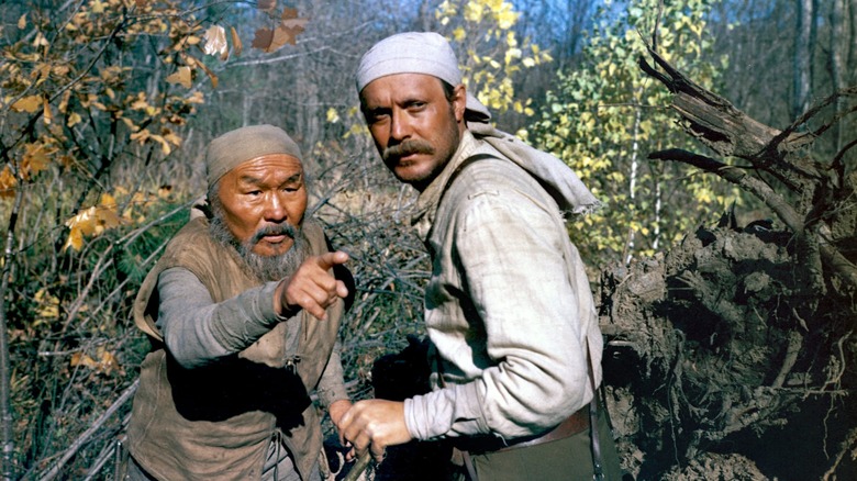 Dersu Uzala pointing at something in the woods whule Yuri turns to look in Dersu Uzala