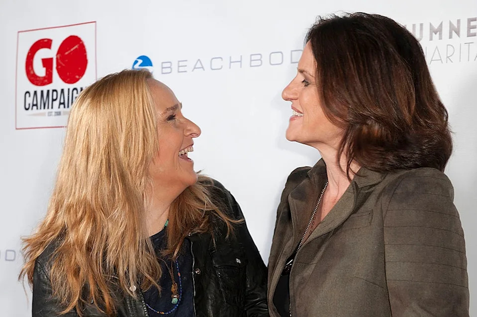 Two people smiling and facing each other at an event; one is wearing a jacket, the other a blazer