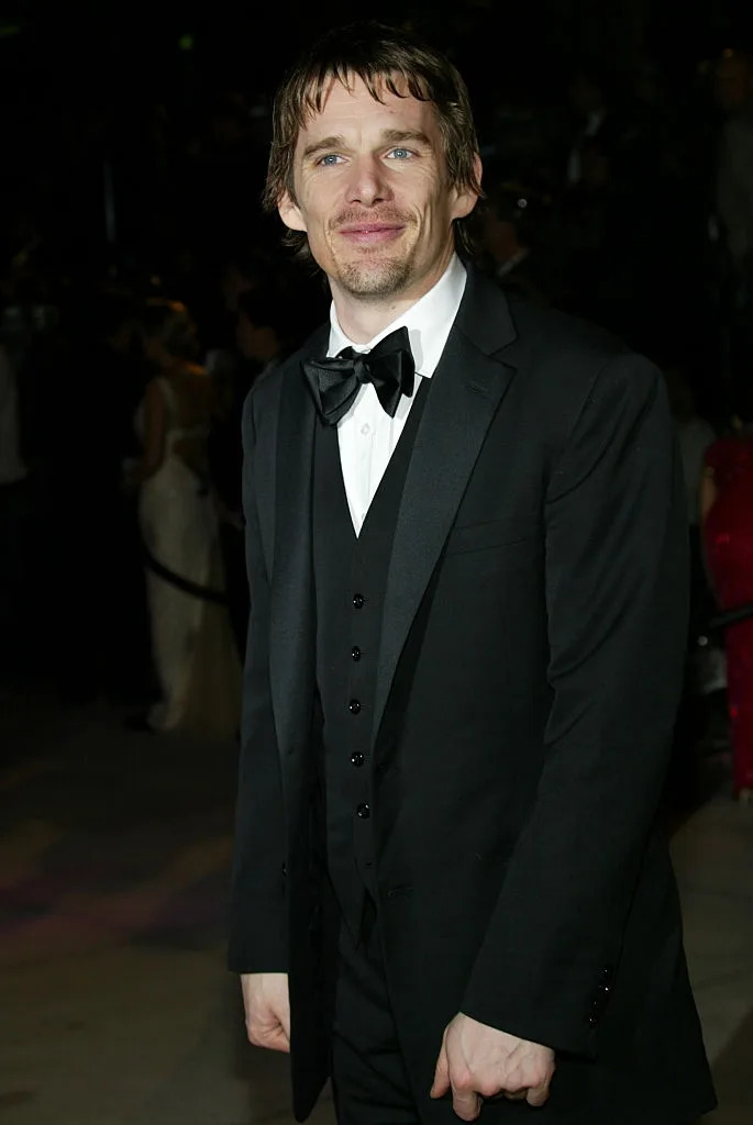 A person on the red carpet wearing a classic tuxedo with a bow tie, smiling at the camera