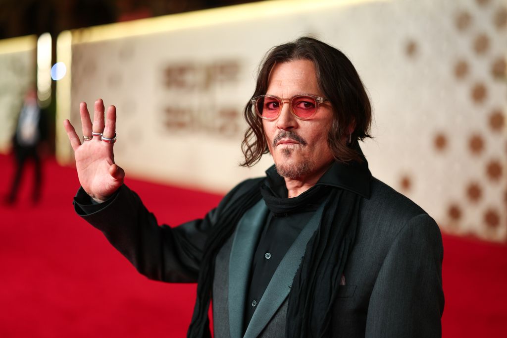 Johnny Depp stands on the red carpet and raises a hand in a wave.