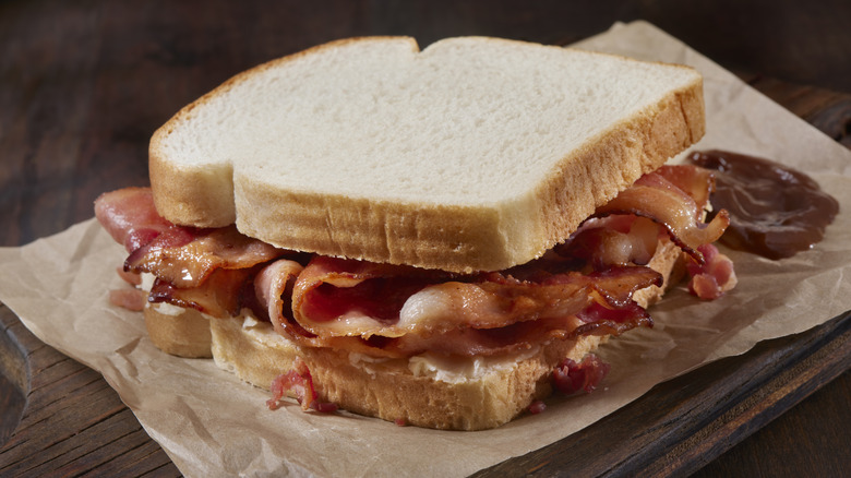 A bacon butty sandwich with sauce on the side set on brown paper