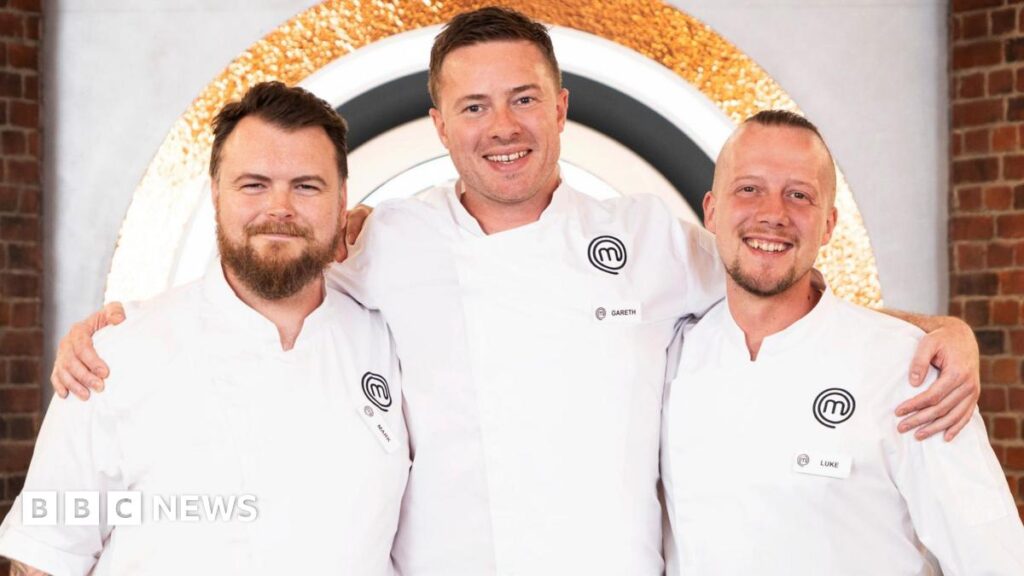 The three finalists from left to right, Mark O'Brien, Gareth Baty and Luke Emmess. All three chefs are wearing white chefs' coats and black trousers. O'Brien has short dark hair and a full beard. Baty, who has his arms round the shoulders of the other two, is taller and has similar short dark hair with light stubble. Emmess has very short dark hair on the top of his head and is shaved at the sides. He has a short goatee beard. They are on the set of MasterChef, with a brick wall and the programme's logos behind them.