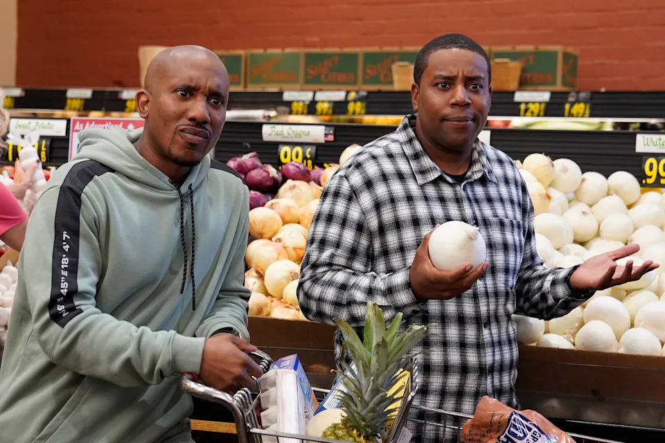 Two people shopping in a grocery store, one holds an onion and looks puzzled