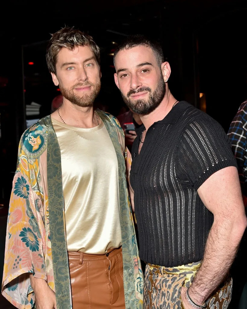 Two individuals on the red carpet; one in a floral kimono and satin top, the other in a black sheer shirt and leopard-print pants