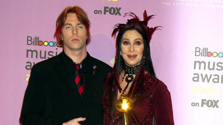 Cher in a maroon outfit beside her son Elijah Blue Allman