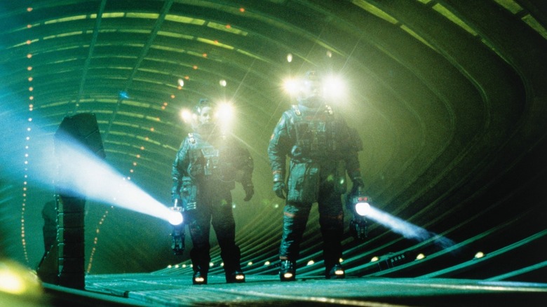 Two astronauts in spacesuits with flashlights walk down a green corridor in Event Horizon