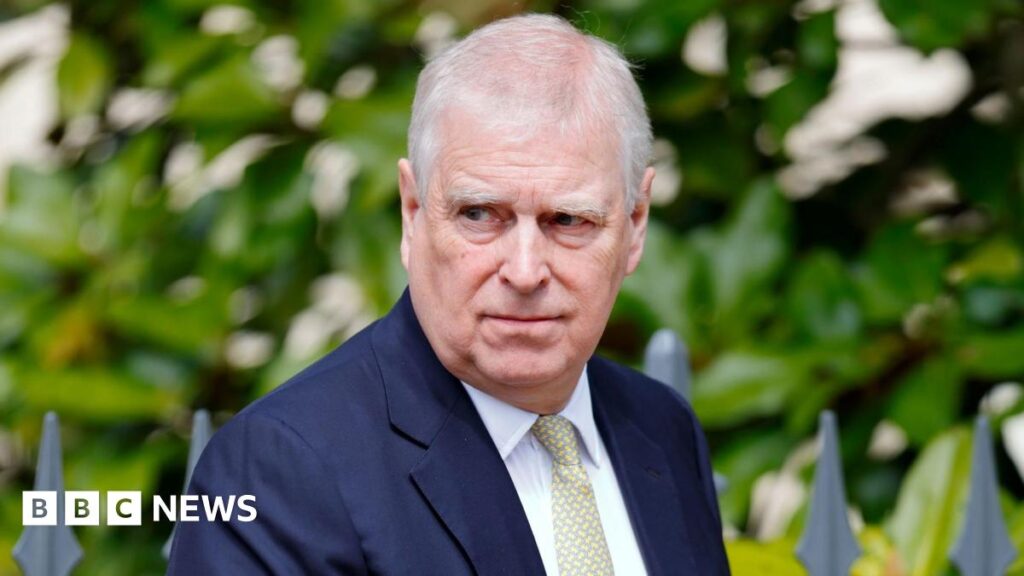 A close-up image of Andrew Mountbatten-Windsor. He is an older man with short white hair. He is wearing a dark blue suit jacket, a white shirt and a pale green and yellow patterned tie. He is looking away from the camera with a neutral expression on his face.