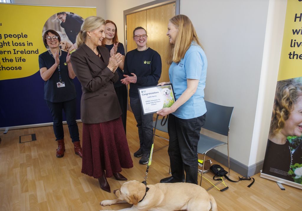 The Duchess of Edinburgh (centre left) presents Judith Martin (right) and her guide dog Brooke with a certificate for being the 1000th active volunteer for Guide Dogs Northern Ireland