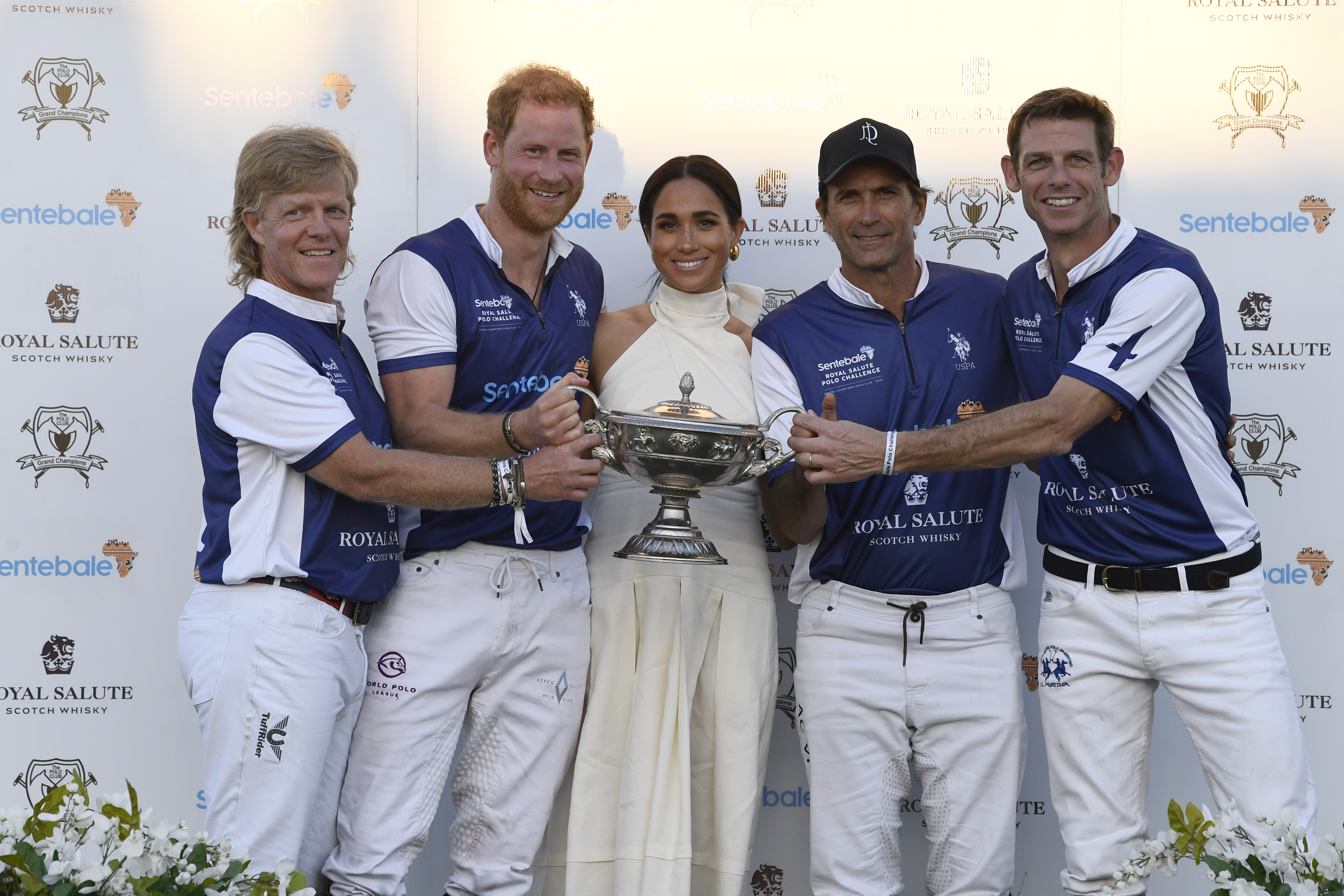 Prince Harry and Meghan Markle posing with a polo team holding a trophy