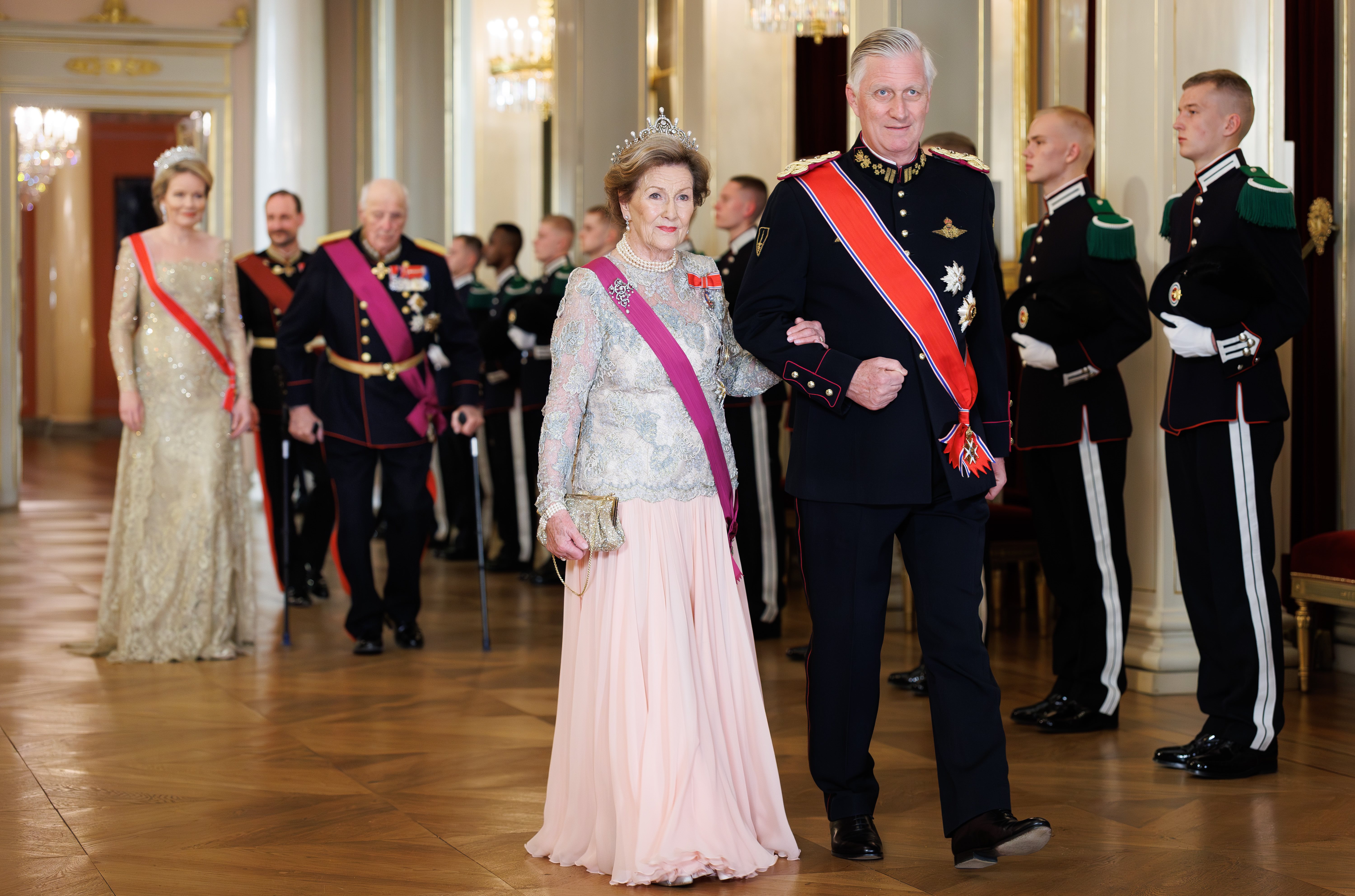 Queen Sonja of Norway wearing a pink gown walking with King Philippe