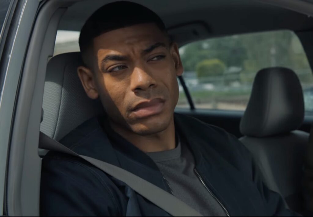 young black man in passenger seat of a car looking pensively out the window.