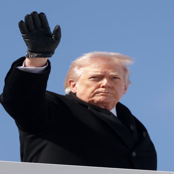 Donald Trump in a coat waves while boarding an aircraft