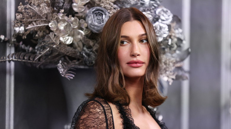 Hailey Bieber with shoulder-length hair standing in front of floral arrangement
