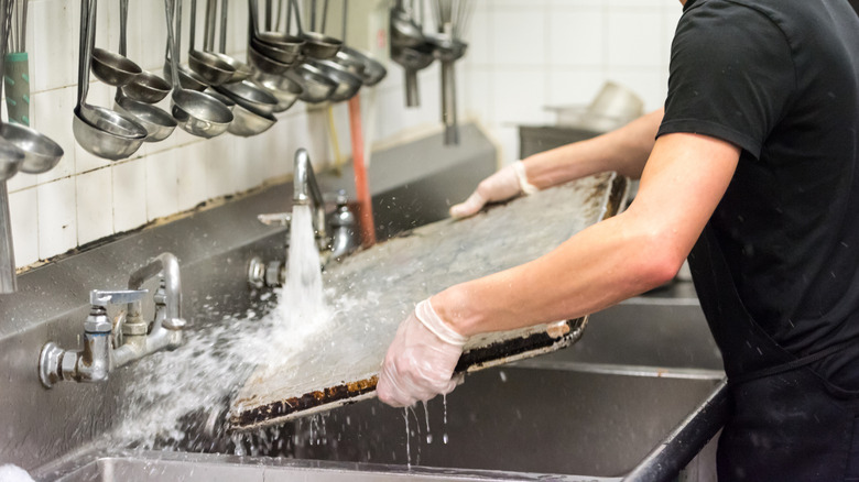 Dishwasher washing sheet pan in restaurant kitchen