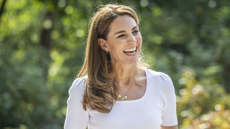 Kate Middleton smiling wearing a white, short-sleeve top while outside