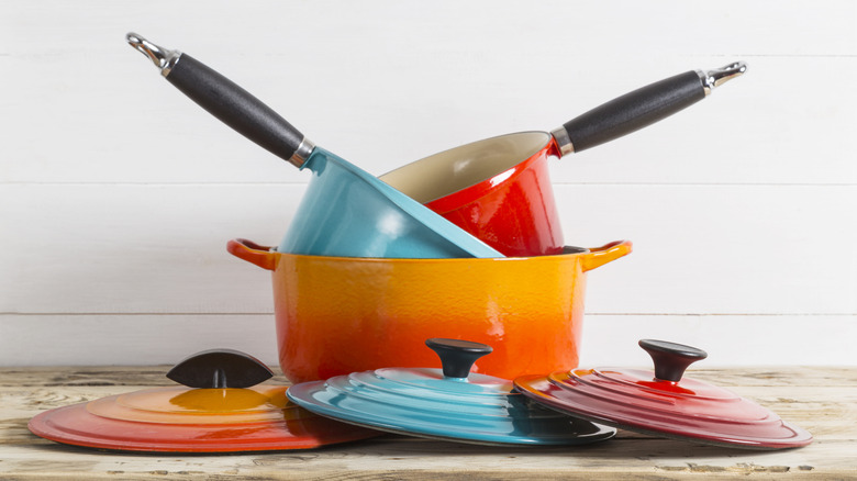Colourful pots, pans and saucepans stacked up on wooden surface with lids in front