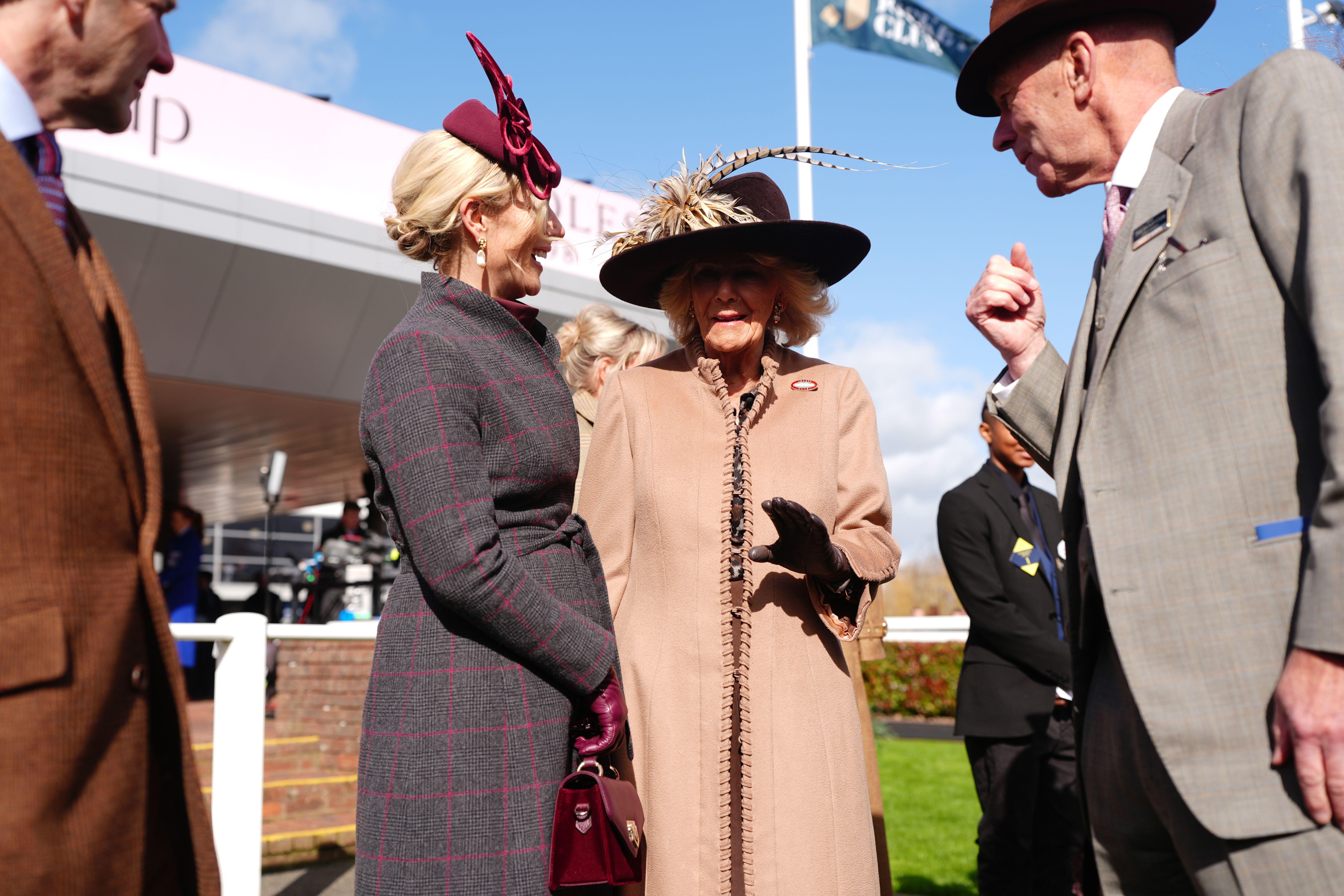 Zara Tindall wearing a gray coat laughing and talking to Queen Camilla at Cheltenham races