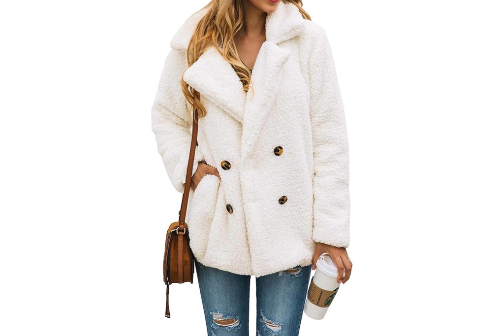 Woman wearing a white faux fur double-breasted coat and distressed blue jeans, holding a brown purse and a white coffee cup.