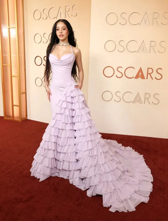Chase Infiniti arrived at the 2026 Oscars wearing a soft lavender Louis Vuitton gown with layered ruffle details and diamond jewelry.