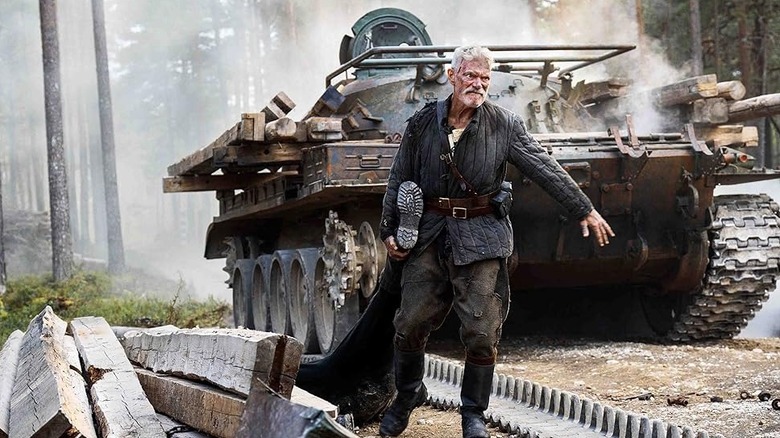 Stephen Lang as Yeagor Draganov dragging a body by a tank in Sisu: Road to Revenge