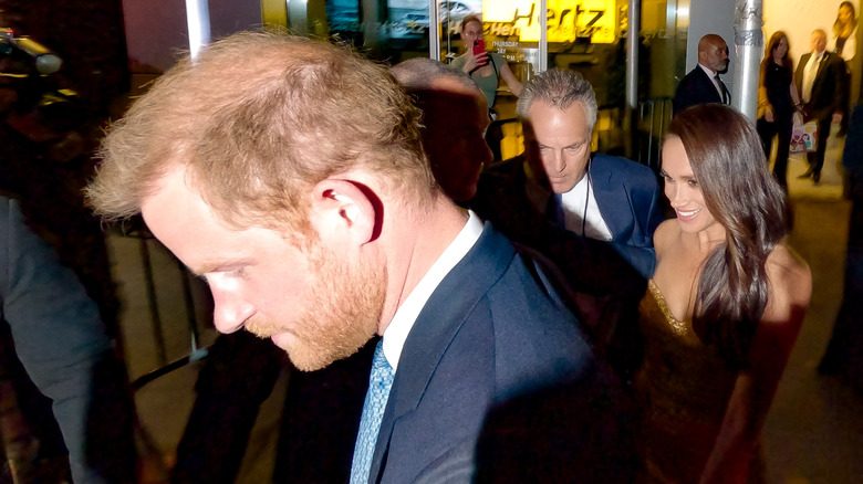 Security escorts Prince Harry, Duke of Sussex and Meghan Markle, Duchess of Sussex through a group of photographers outside The Ziegfeld Theatre (2023)