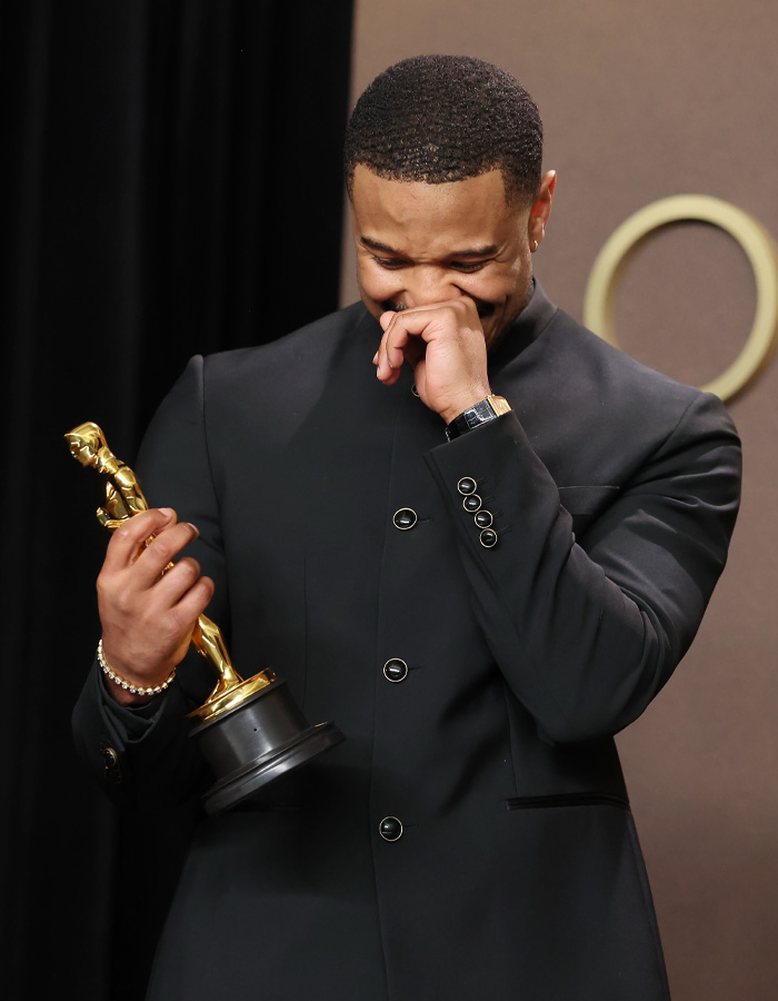 Michael B. Jordan holding an Oscar, dressed in black, reacting emotionally during a post-Oscars moment.