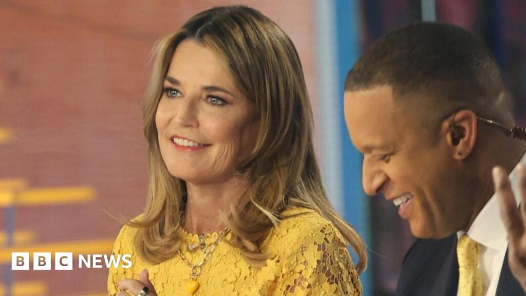 Savannah Guthrie is on the left, wearing a yellow dress and smiling. Her suited male co-host is looking down and smiling, on the right of the image.