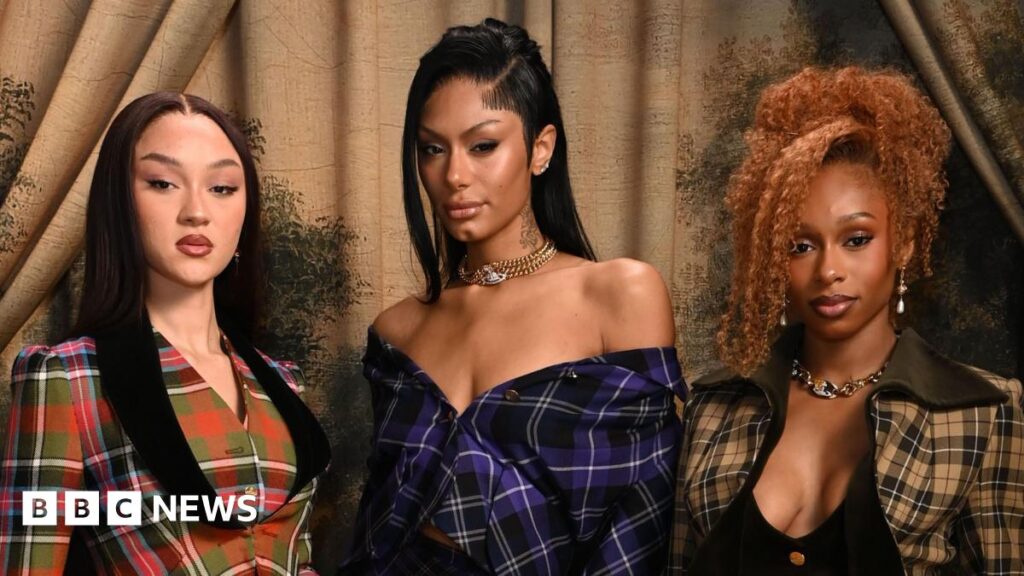 Flo: The girl group on entering into their ‘bombastic’ era Stella Quaresma is on the left in a red and green tartan blazer. Jorja Douglas is to the middle in a black and purple tartan off-the-shoulder dress. Renee Downer is on the left in a black and green tartan jacket which she is wearing over a black top.