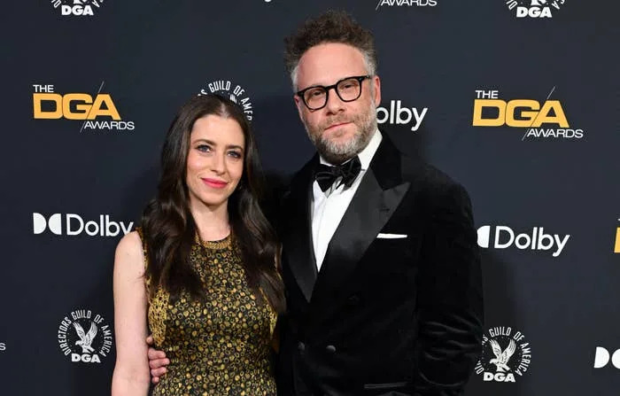 A man in a tuxedo and a woman in a sleeveless, patterned gown pose together on the red carpet at the DGA Awards