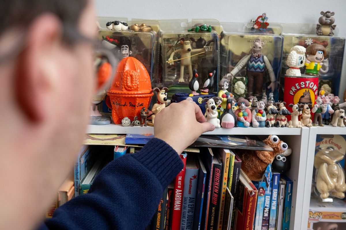 An individual wearing glasses and a blue long-sleeved shirt is reaching for a figurine on a shelf adorned with various books and decorative items.