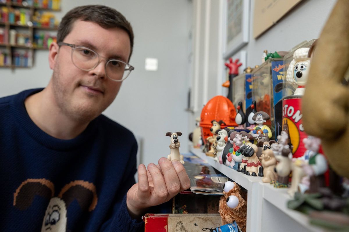 An individual, wearing glasses and a blue long-sleeve shirt, stands in a room adorned with shelves displaying an assortment of figurines and decorative items.