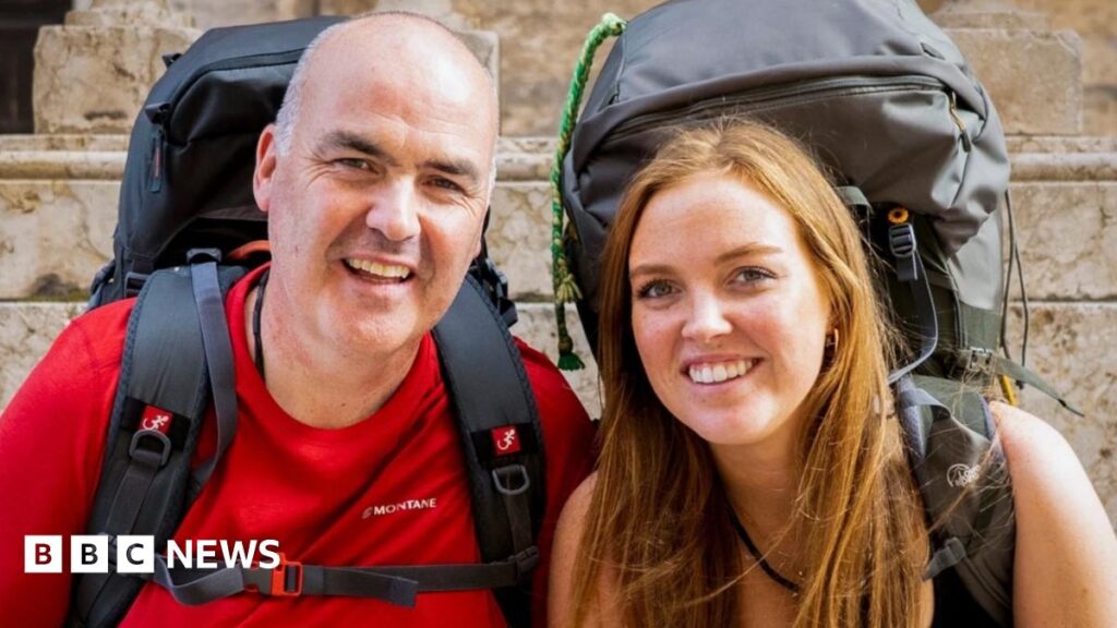 two people looking at the camera - they are a bald man and a red-headed woman. Both are wearing big rucksacks