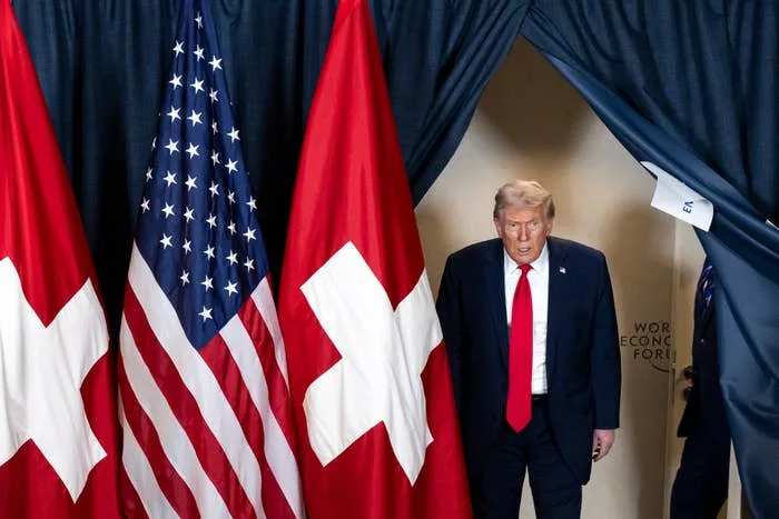 A person in a suit walks through curtains adorned with Swiss and American flags at the World Economic Forum