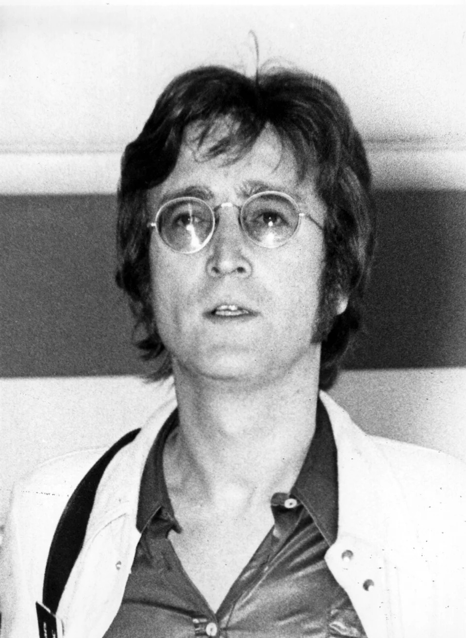 Person with medium-length hair and glasses wearing a collared shirt and jacket, posing calmly. 