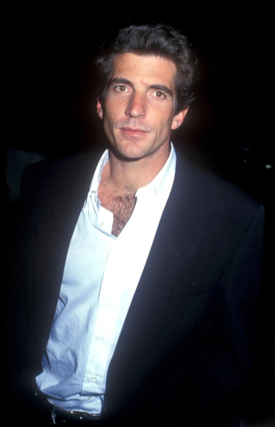 A person in a dark suit and white open-collar shirt at a public event